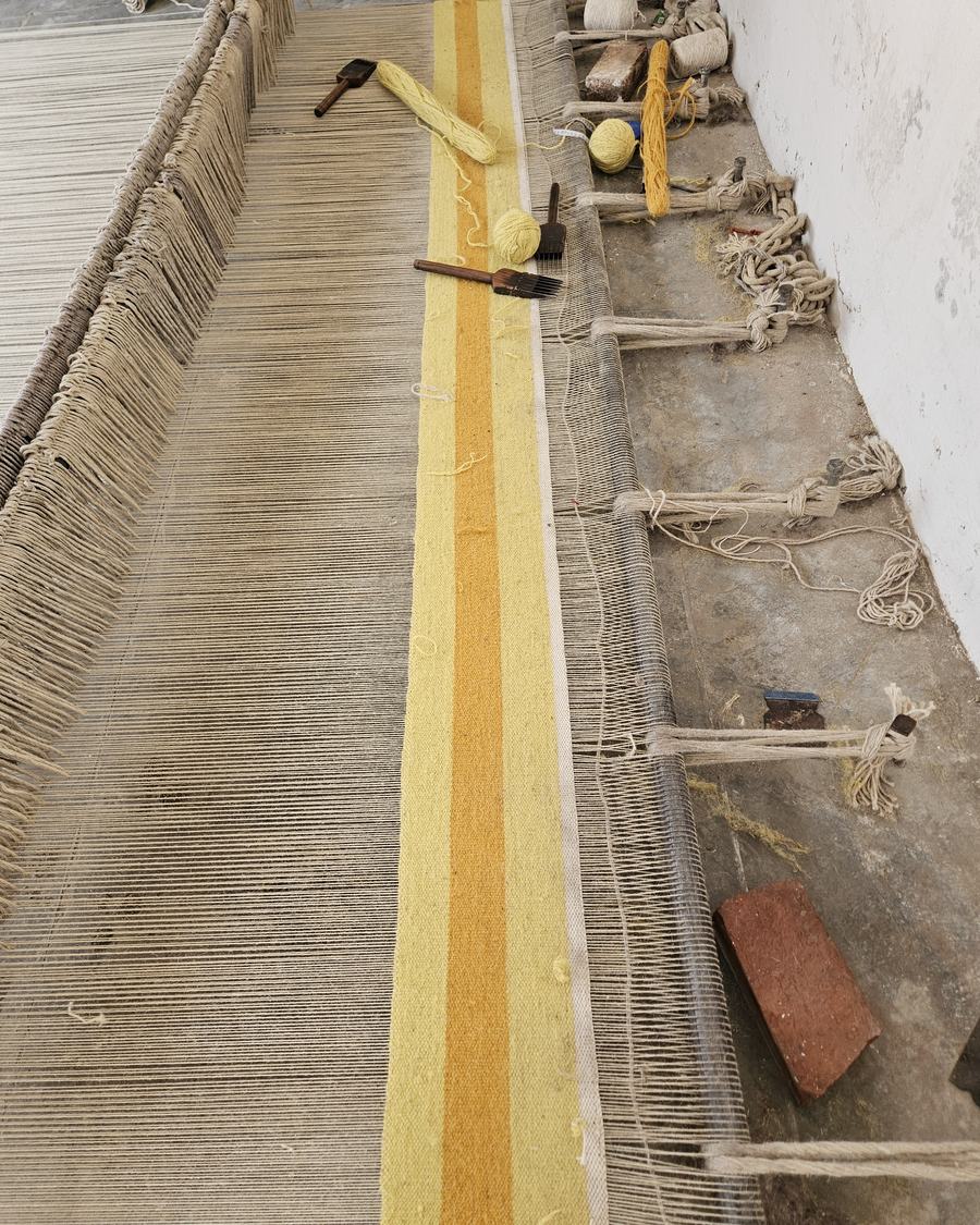 A yellow-striped flatweave runner half-woven on the loom in the Rug Gossips workshop